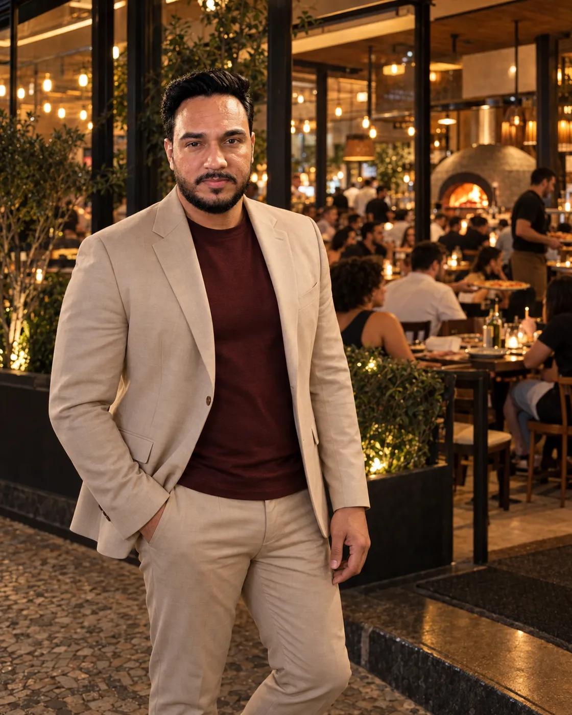 Leonardo Viana, fundador da Gestão Restaurante, de terno bege na entrada de um restaurante cheio, com o salão e o forno a lenha ao fundo.